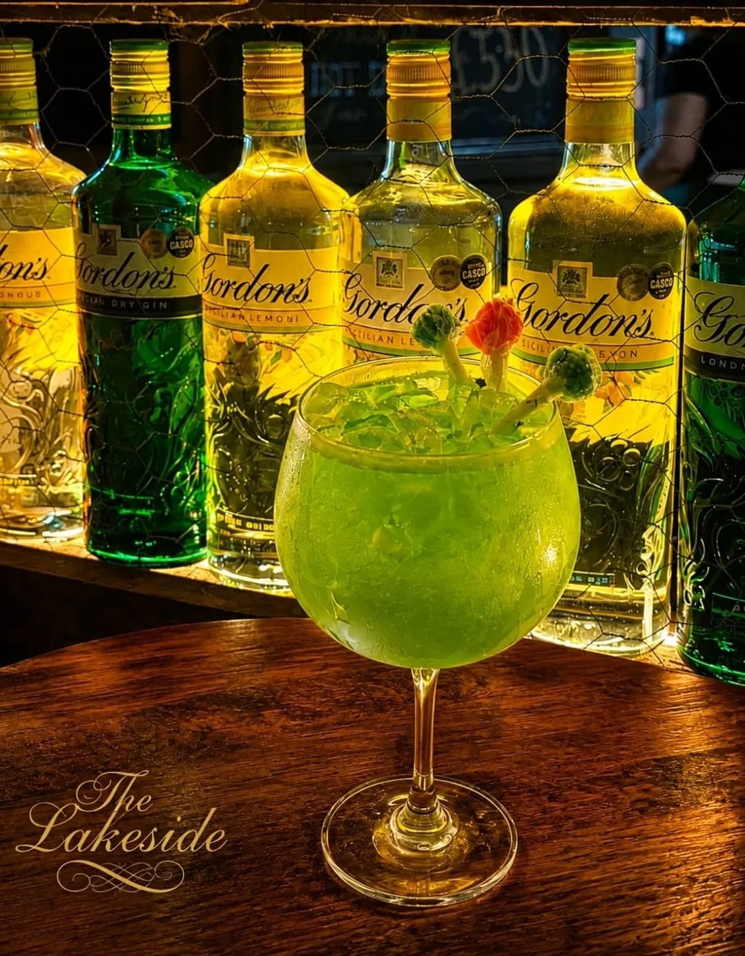 A green gin cocktail with sweet garnishes on a wooden table at the gin bar of The Lakeside
