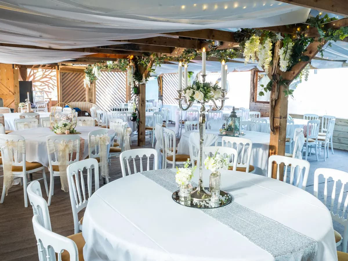 Round tables dressed in white linen with silver candelabra, florals and chair sashes set for a wedding under the draped marquee at The Lakeside Inn