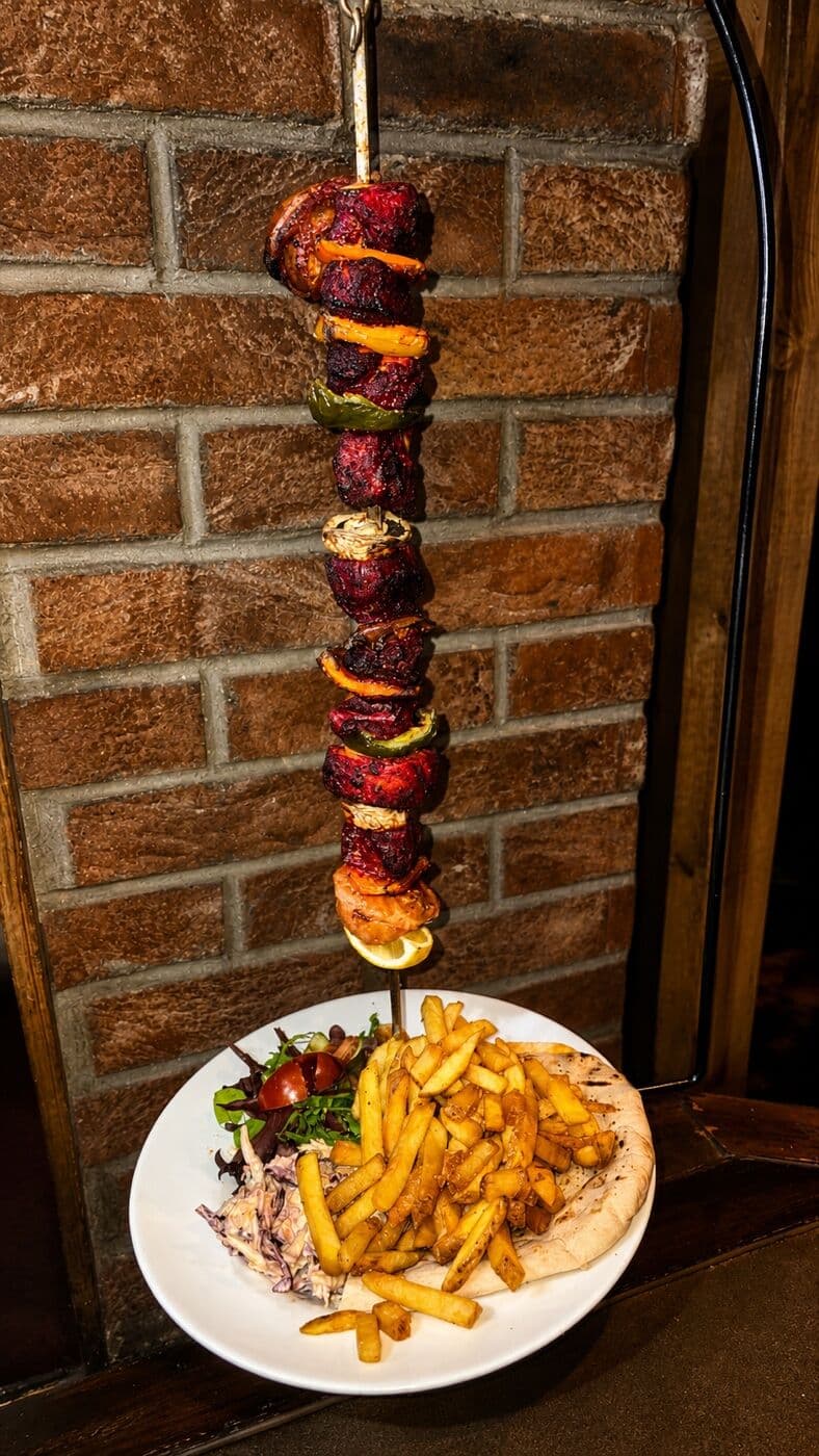 A hanging char grilled kebab skewer served over chips and flatbread at The Lakeside Inn