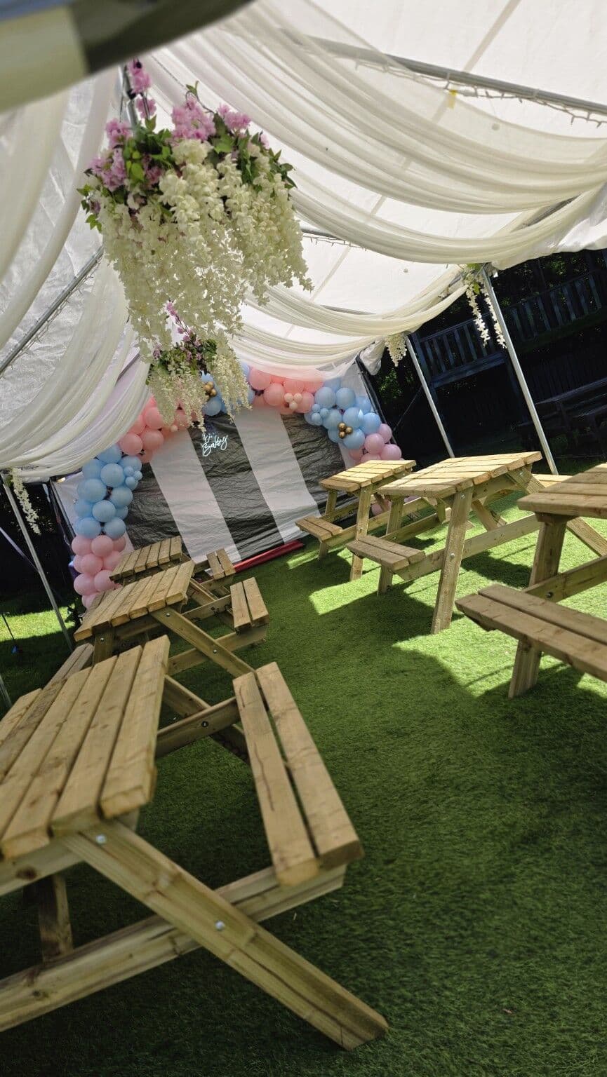 The outdoor marquee at The Lakeside Inn dressed for a daytime celebration, with a pink and blue balloon arch, florals and picnic benches on the lawn