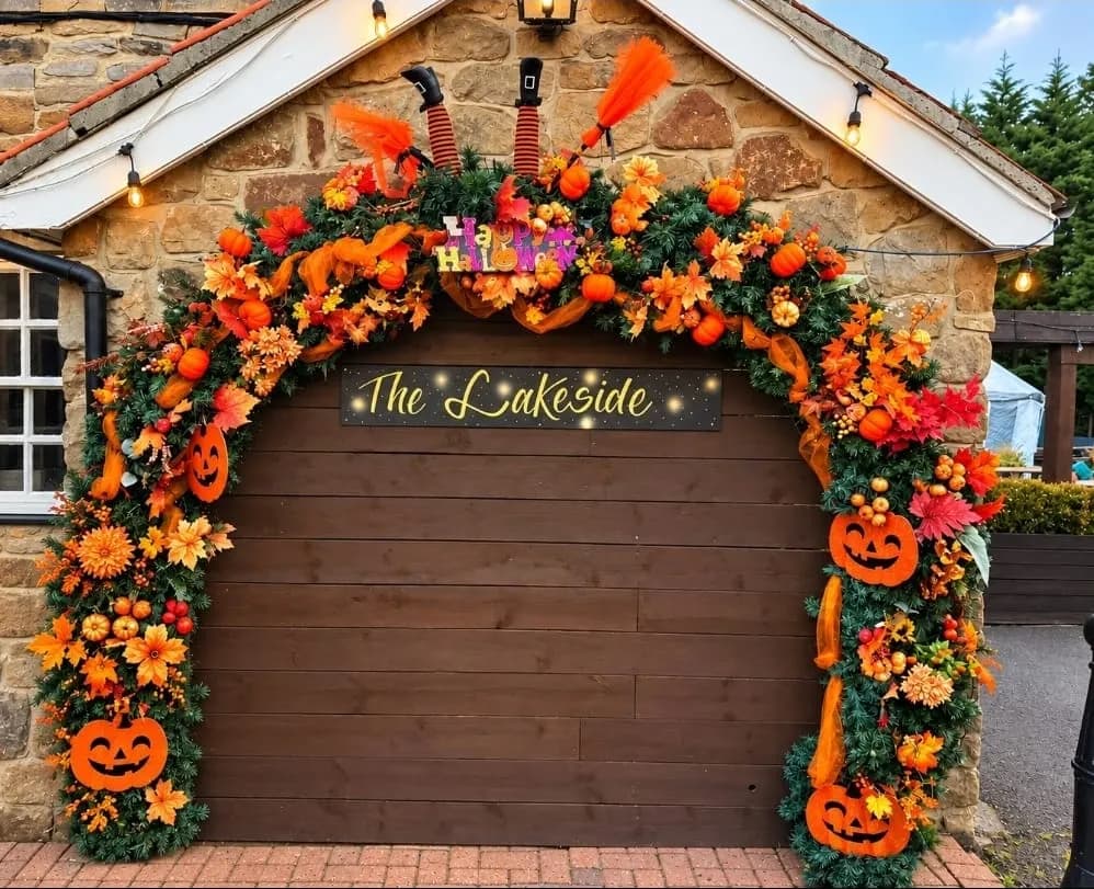 A Halloween garland of autumn leaves, pumpkins and jack o' lanterns around The Lakeside sign, with a witch's legs peeking over the top